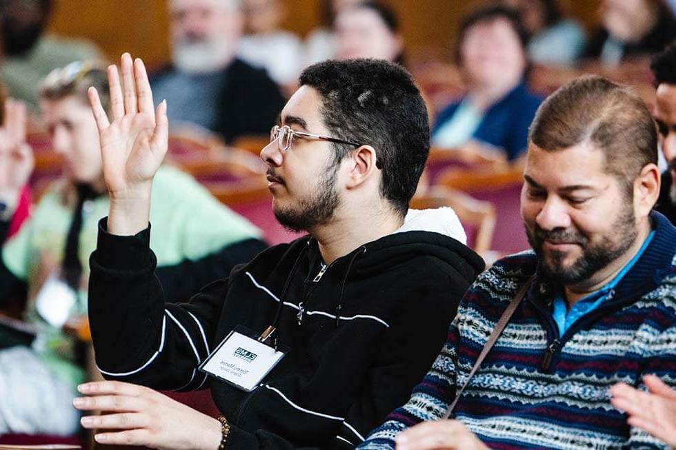 Photo of male student raising his hand sitting in Berchmans Hall, Veritas Auditorium